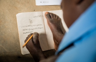 Djevojčica piše u bilježnicu držeći olovku lijevom nogom