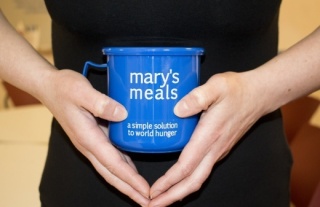 Ženske ruke drže plavu šalicu na kojoj piše Mary's Meals